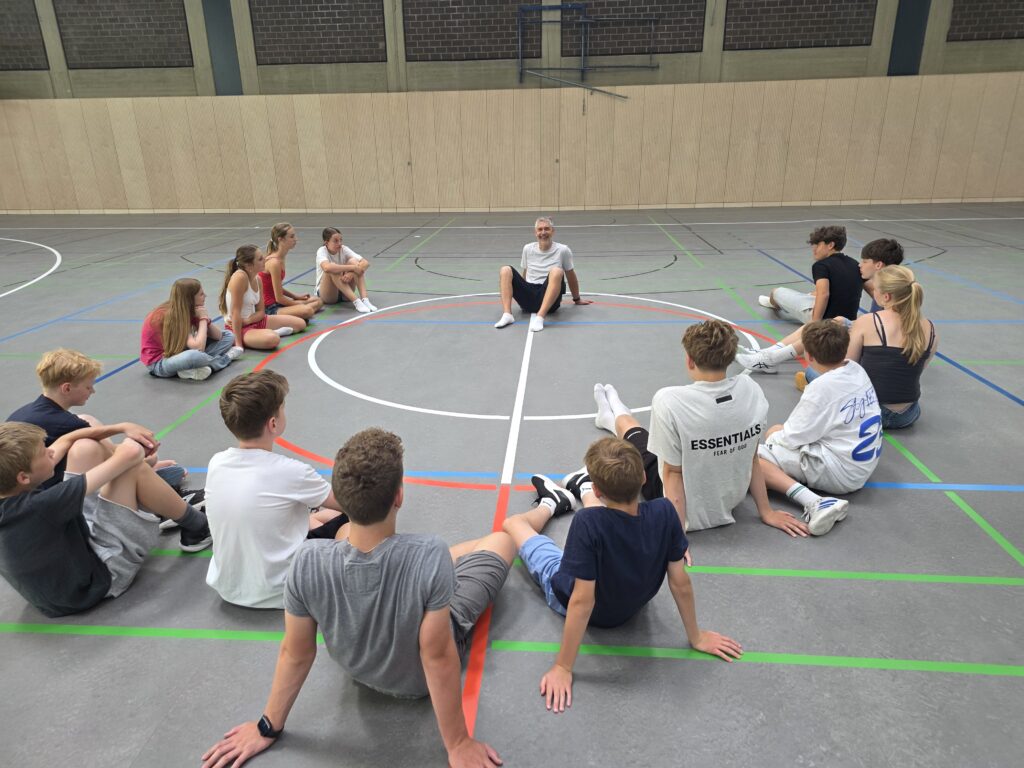 Sporthelferprojekt sitzt im Sitzkreis in der Sporthalle